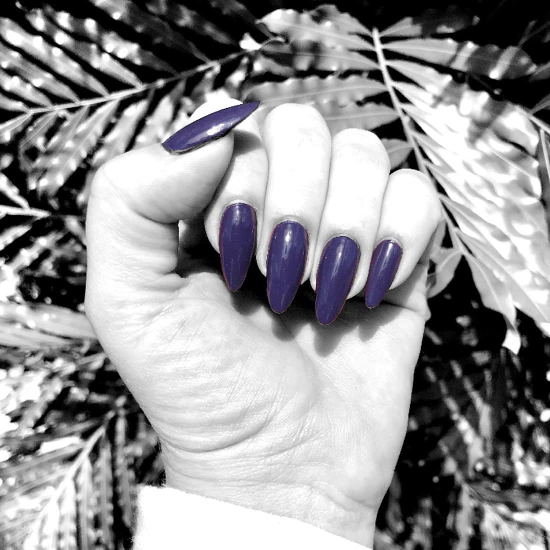 Purple stiletto nails against palm leaves, manicured at McAllister Spa near South Beach