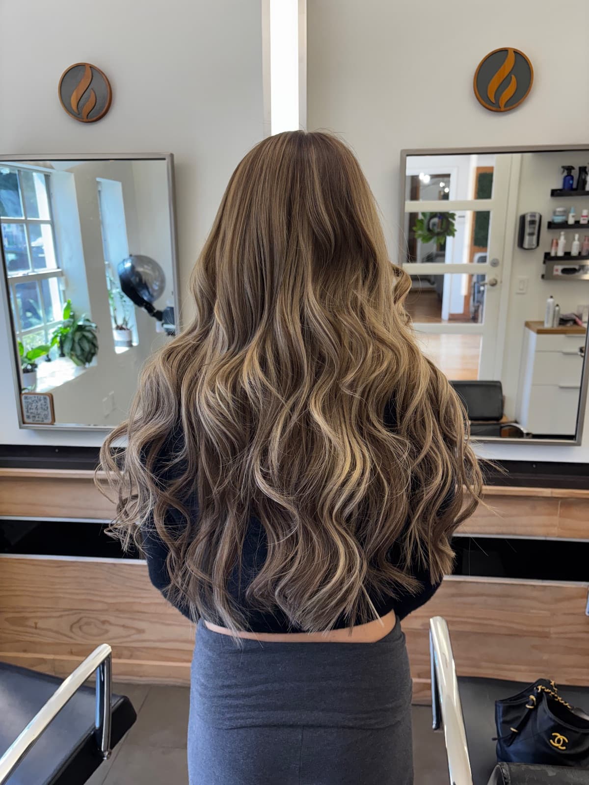 Waist-length bronde color, cool ashy ribbons drawn through a warm brown base and waved from the mid-lengths down — hair extensions and balayage by Hali at McAllister Spa in Miami Beach