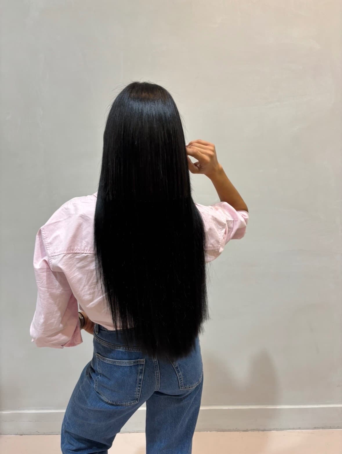 After: sleek jet-black hair falling straight past the waist, the added length blended invisibly into her own — hair extensions by Hali at McAllister Spa in South Beach